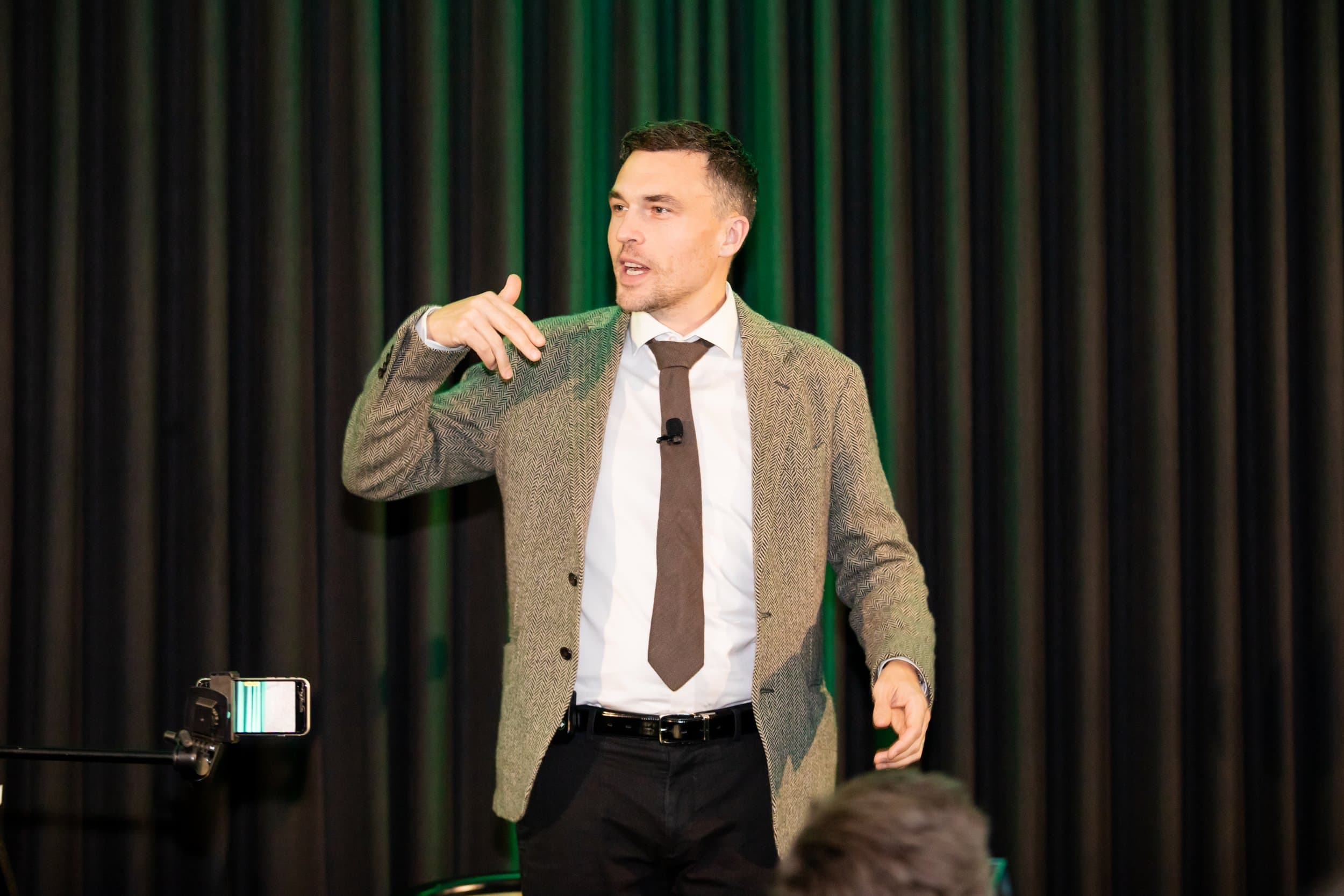 Andy Nunn speaking on stage in front of green curtains