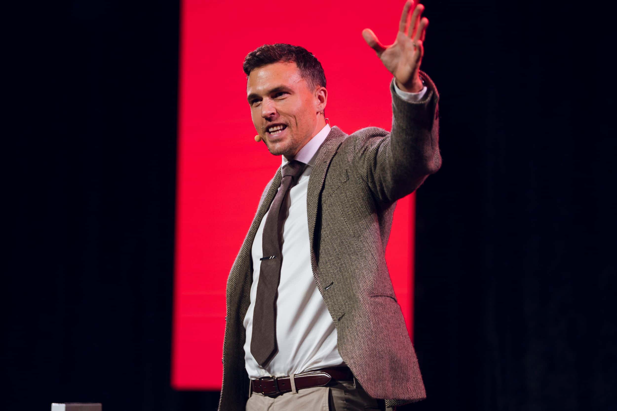 Andy Nunn gesturing during a keynote against a red stage backdrop