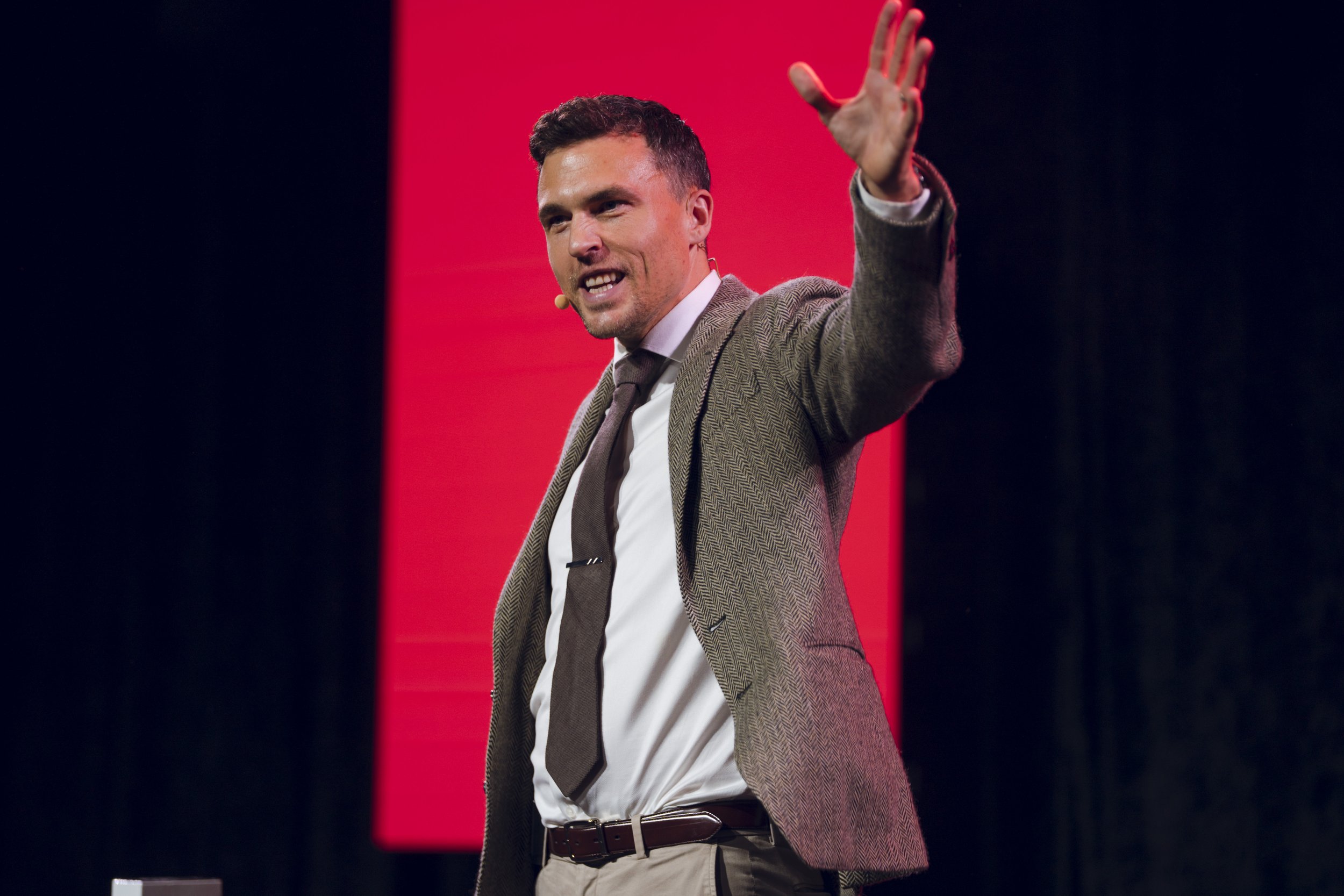 Andy Nunn gesturing during a keynote against a red stage backdrop
